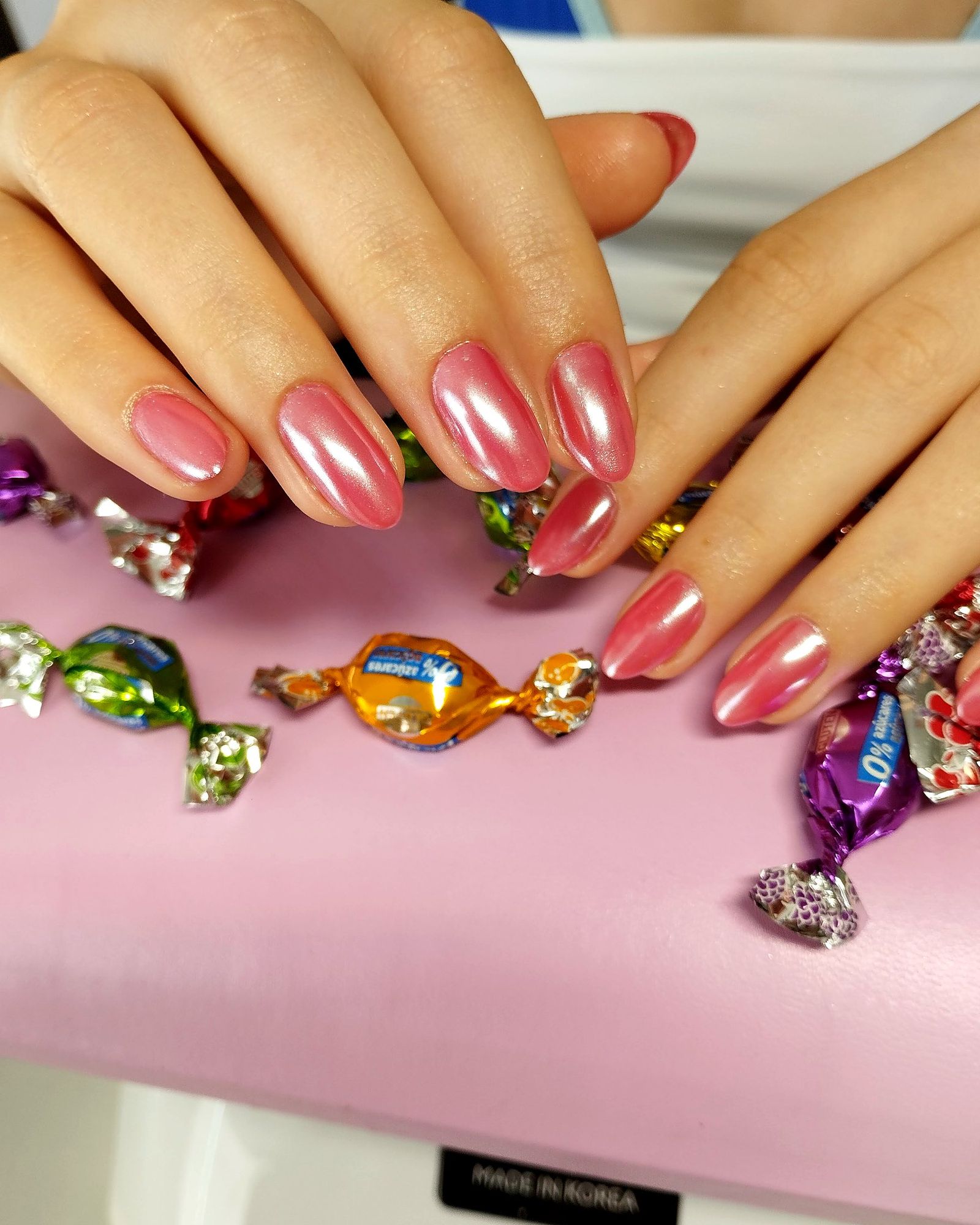 Uñas almendradas en rosa cromado sobre el cojín de manicura, con caramelos